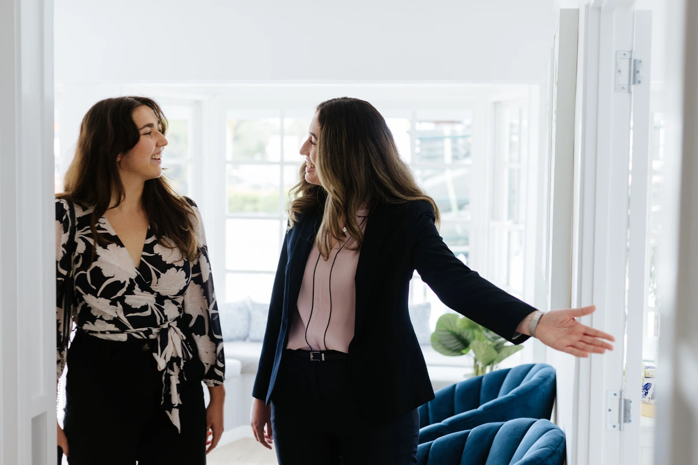 long haired brunette ushering smiling woman into home