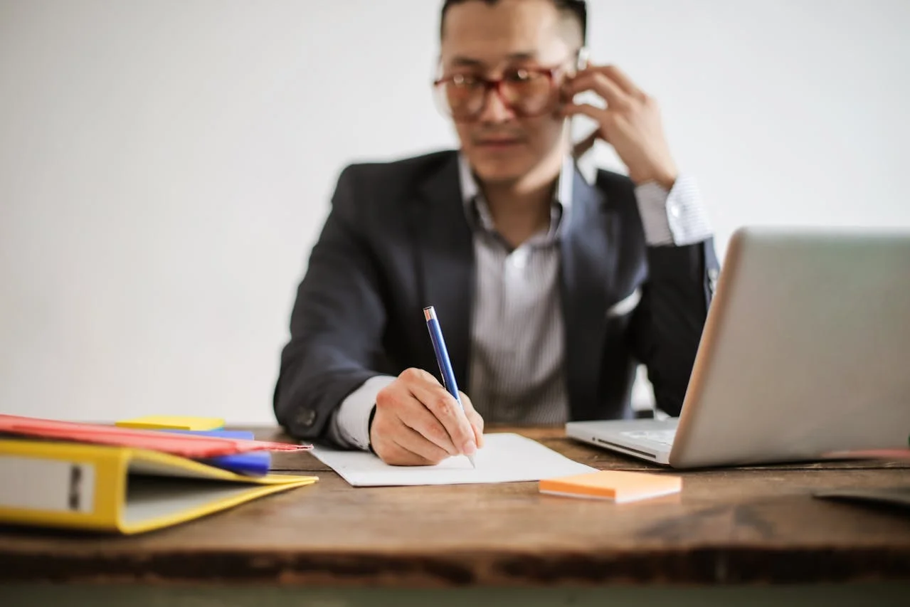 Asian man on phone and writing on paper