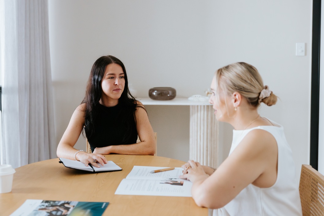 female legal professional with long brunette hair talking to blond haired woman